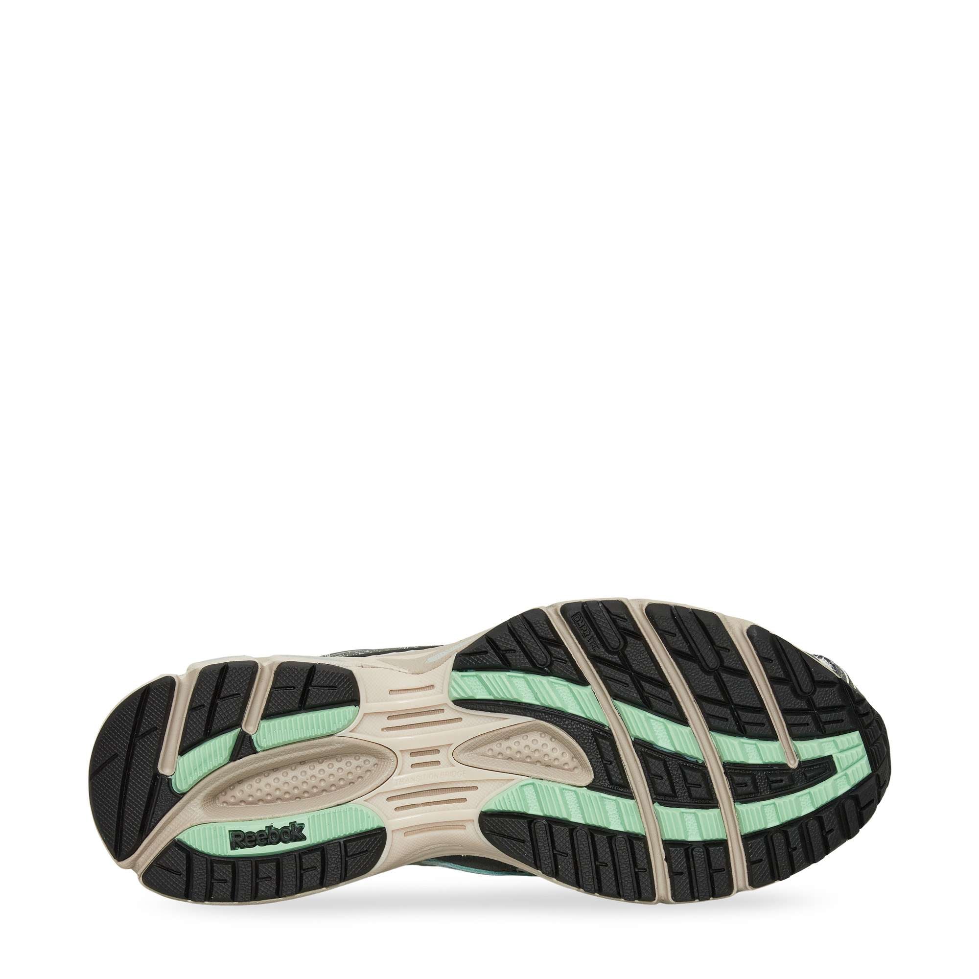 The image shows the sole of a Reebok sneaker. The sole features a beige base with black and mint green rubber tread patterns for traction and flexibility. The Reebok logo appears near the heel area.
