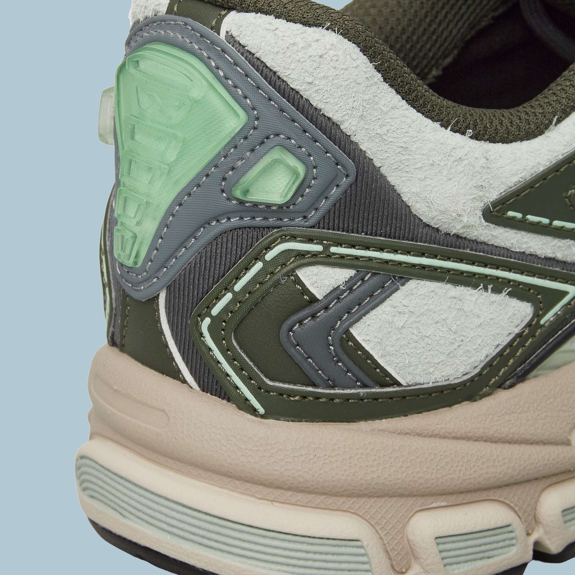 Close-up of the heel of Reebok Premier Road Ultra Shoes, featuring textured white, green, and gray panels with pale green accents and a beige dual-density midsole, set against a light blue background.