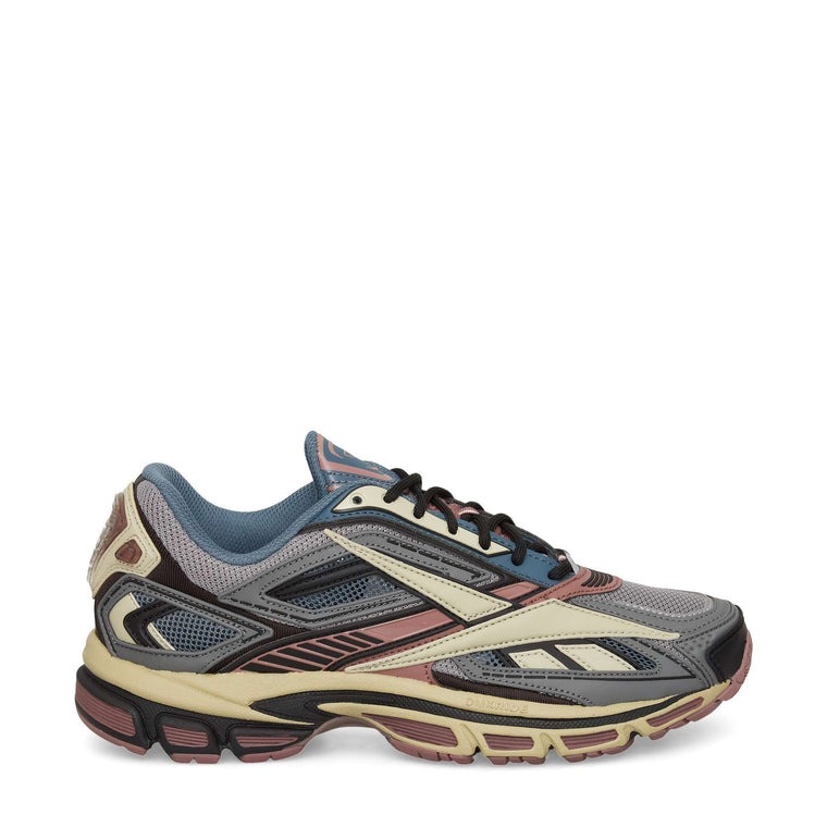 A multicolored athletic sneaker with a mesh upper in gray and blue, accented with cream, burgundy, and black details. The shoe features a chunky, textured sole and layered panel design.