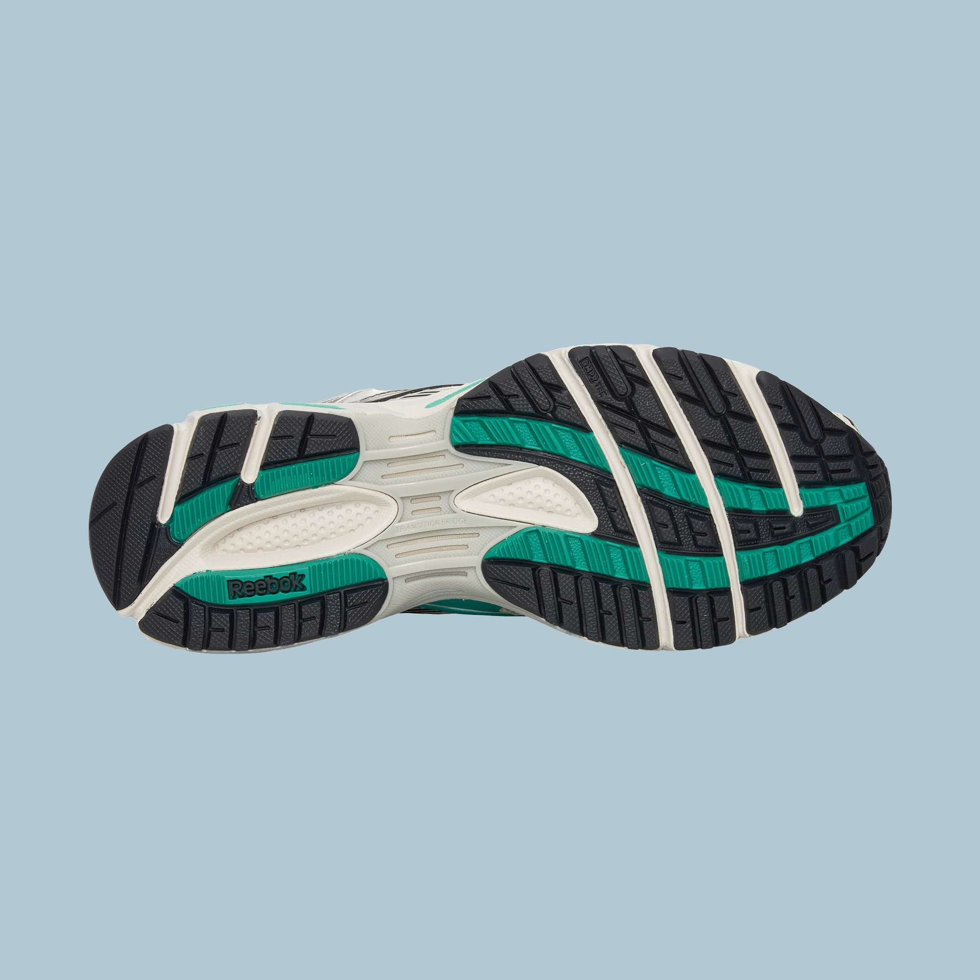 The image displays the sole of the Reebok Premier Road Ultra Shoes, featuring a white base with black and teal tread patterns and Reebok branding, set against a light blue background.