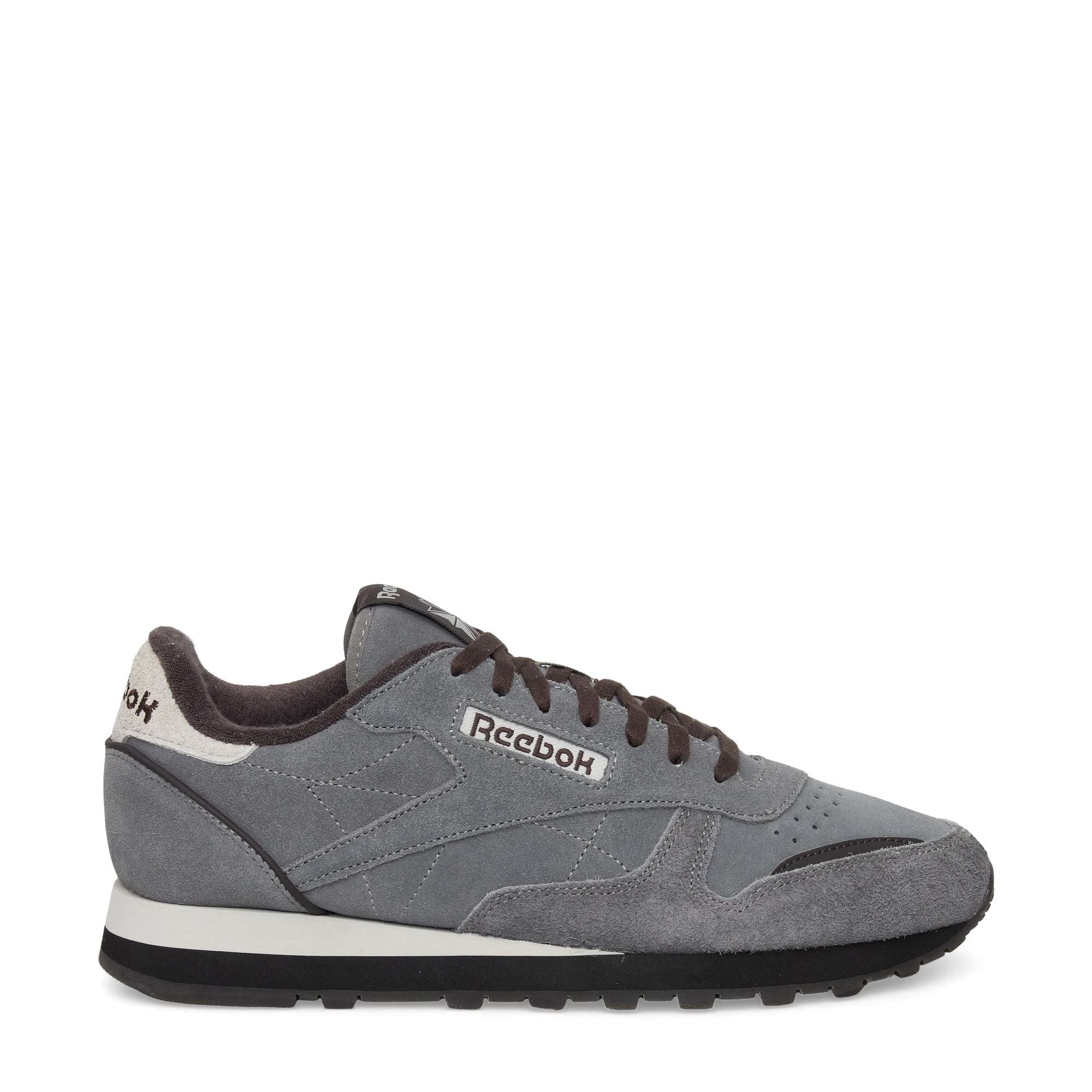 A gray Reebok classic sneaker with black laces, white and black accents, and a black rubber sole, viewed from the side on a white background. The Reebok logo is visible on the side and heel.