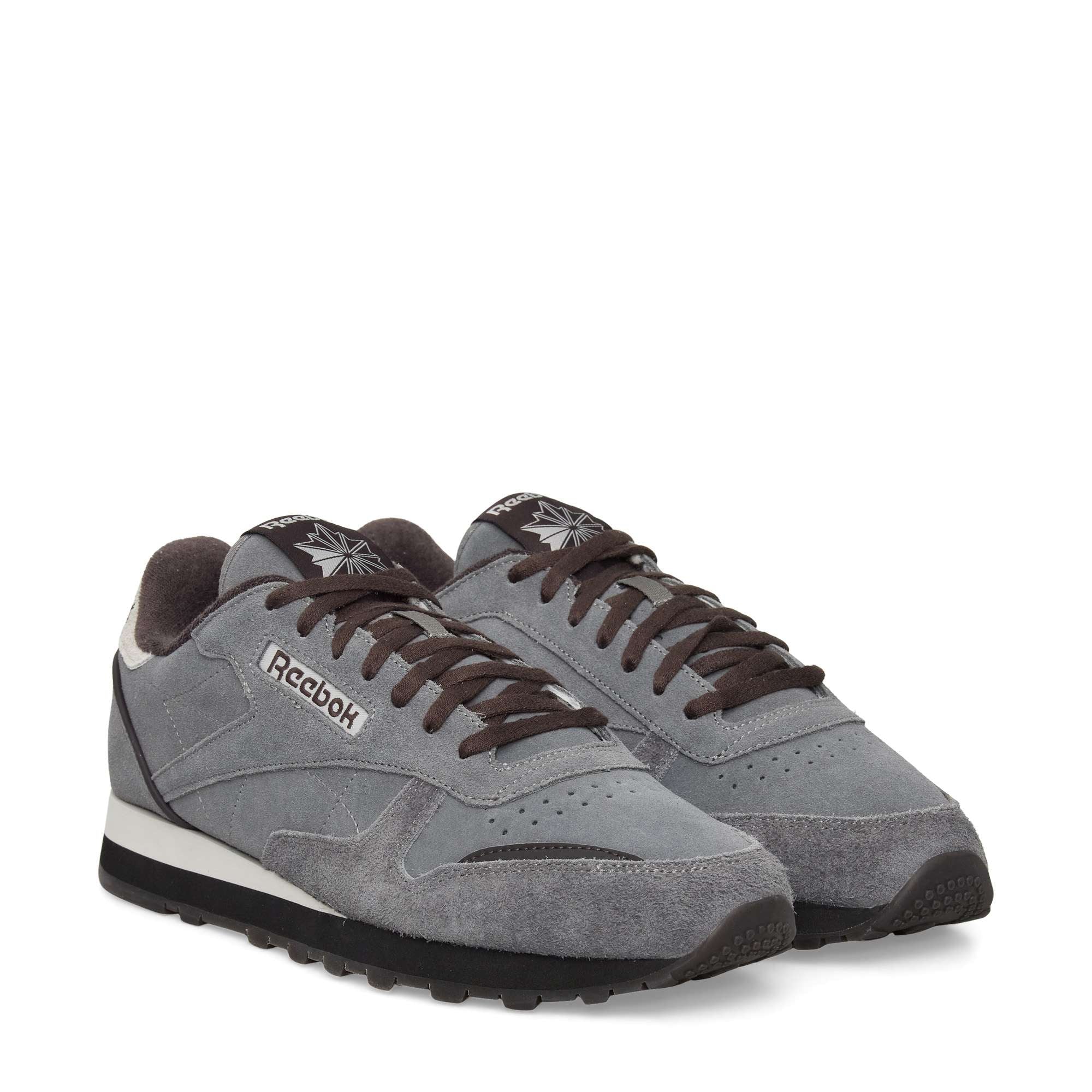 A pair of gray Reebok classic sneakers with black soles, dark gray laces, and white accents. The shoes have a suede and mesh texture with the Reebok logo on the side.