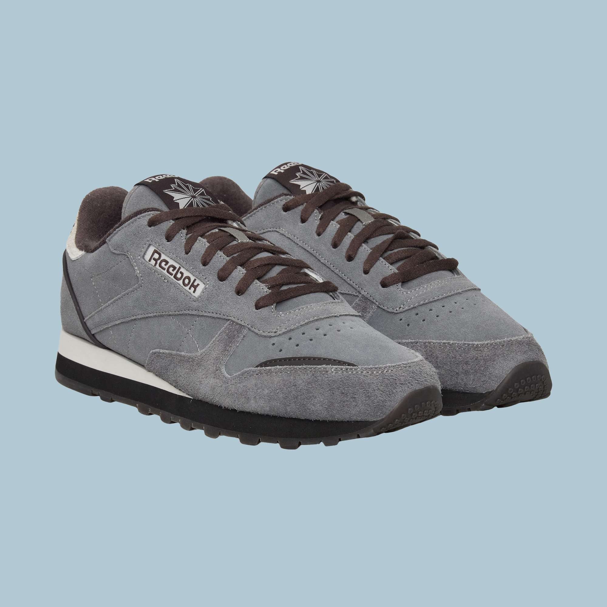 A pair of gray Reebok Classic Leather Premium LTD Shoes with black laces and soles, white midsoles, and suede uppers, featuring a classic silhouette on a light blue background.