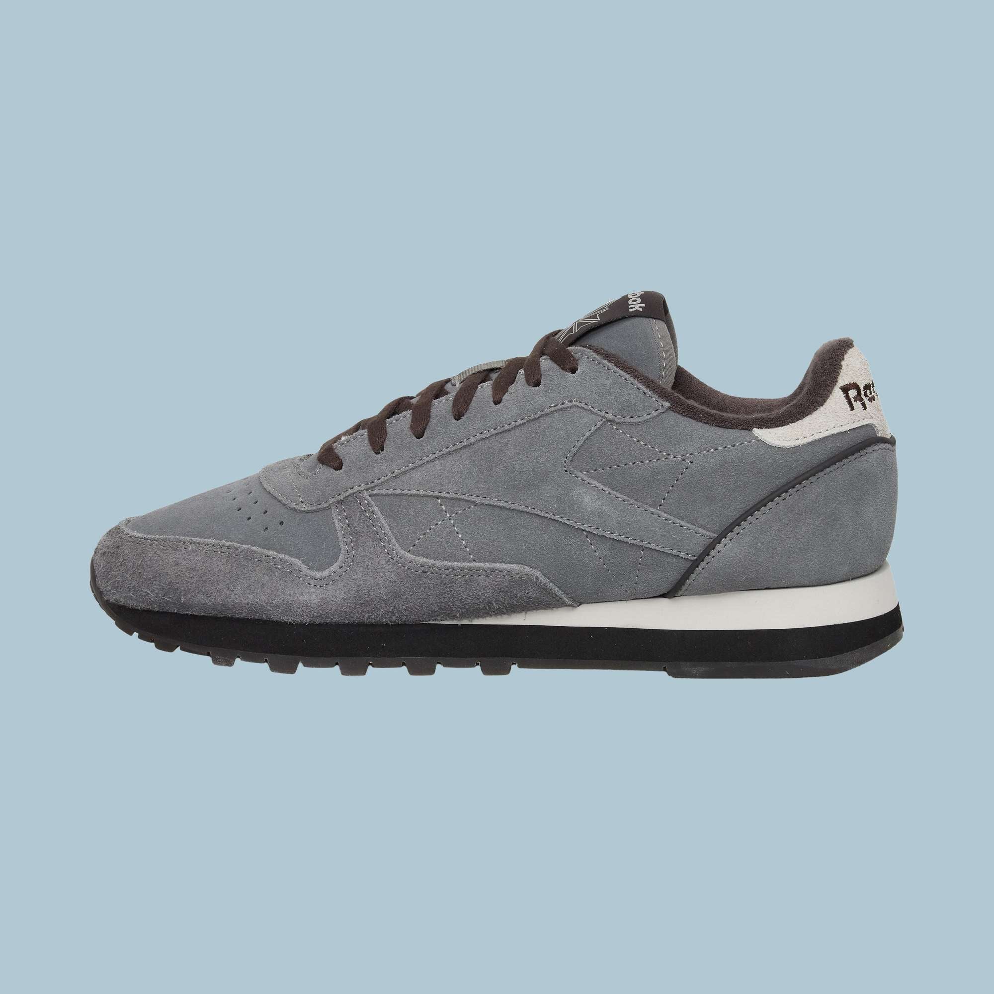 The Reebok Classic Leather Premium LTD Shoes feature gray suede uppers with black laces and sole, a white heel accent, and visible stitching—perfect for fans of classic style. Shown here on a light blue background.