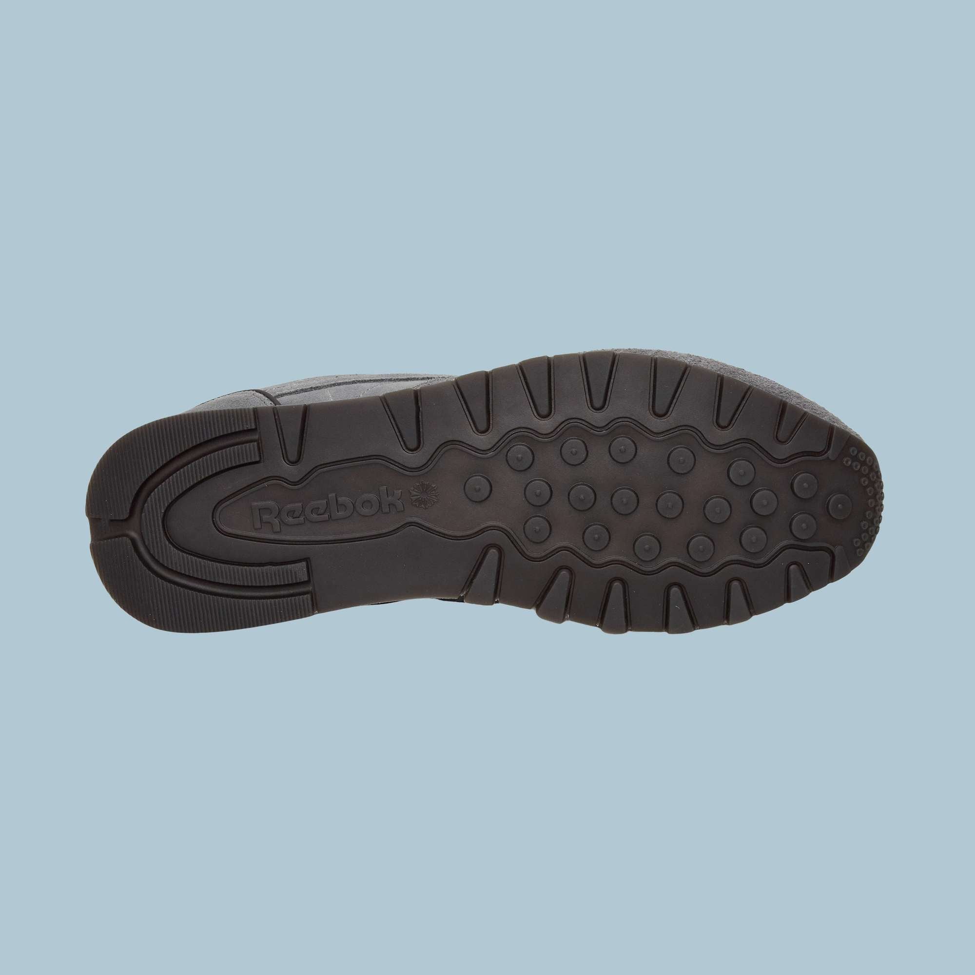 The image displays the black rubber sole of Reebok Classic Leather Premium LTD Shoes facing up on a light blue background, highlighting the textured tread pattern, classic silhouette, and visible Reebok logo.