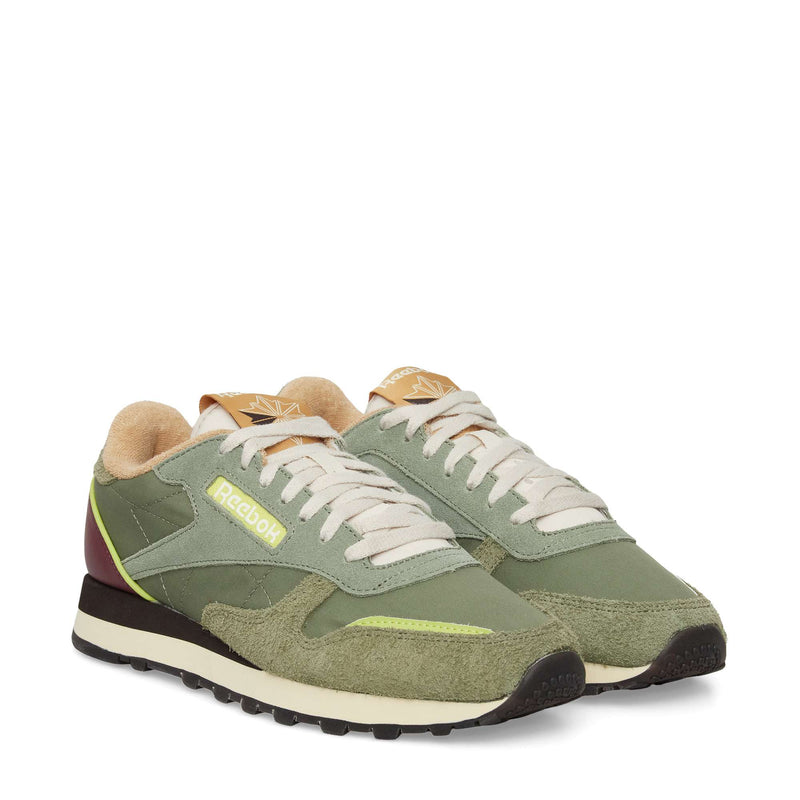 A pair of Reebok Classic Leather Premium LTD Shoes in green with cream laces, suede and leather accents, yellow logos, and black-brown outsoles are displayed side by side on a white background.