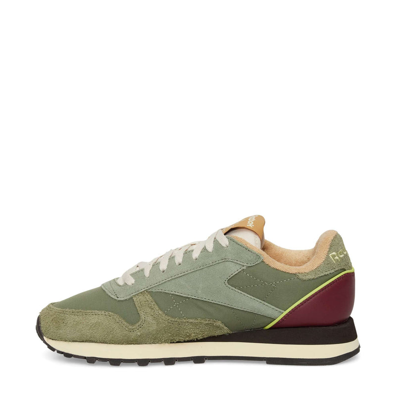A side-profile view of the Reebok Classic Leather Premium LTD Shoes features green suede and fabric uppers, white laces, beige lining, a black and white sole, and a burgundy heel accent—a fresh update on the classic silhouette.