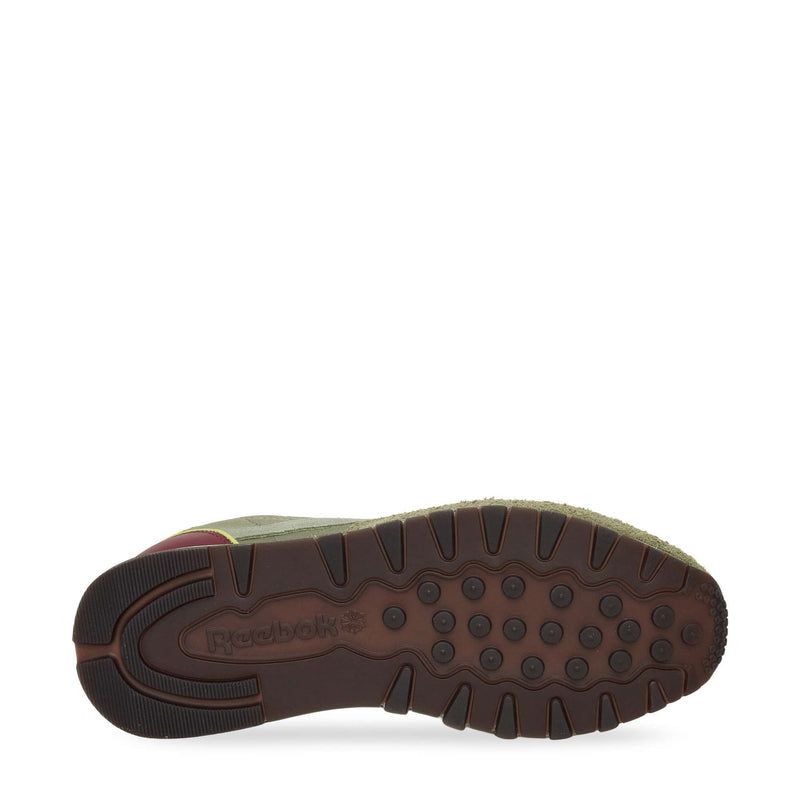 The image shows the bottom view of Reebok Classic Leather Premium LTD Shoes with a brown rubber sole featuring circular treads and the Reebok logo. The retro sneakers have a green upper and a touch of maroon near the heel.