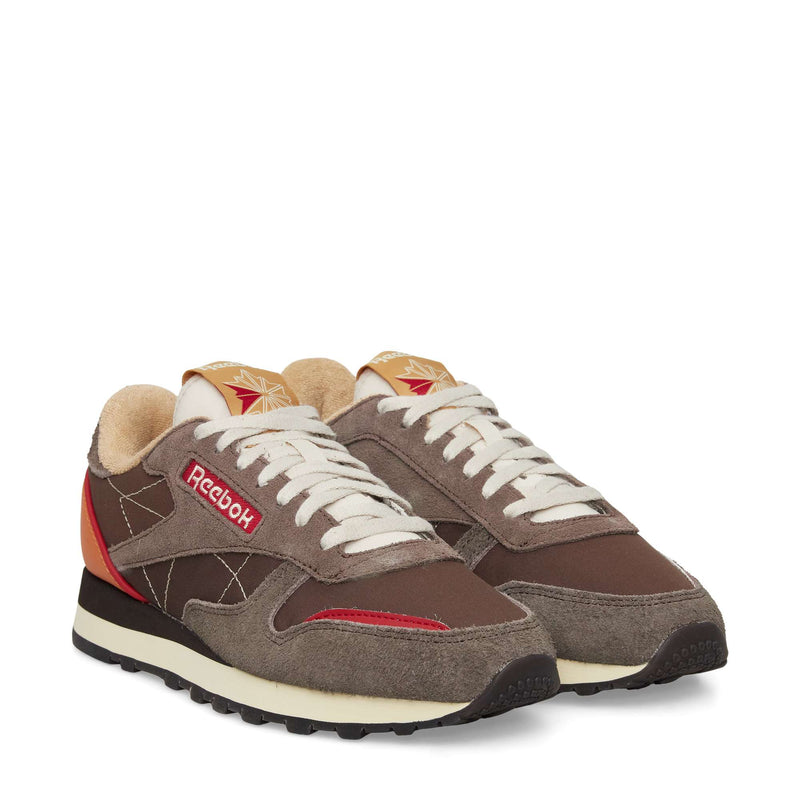 A pair of Reebok Classic Leather Premium LTD Shoes in brown with beige, red, and cream accents. These retro sneakers have white laces, a suede and mesh upper, chunky black sole, and the iconic Reebok logo on the side.