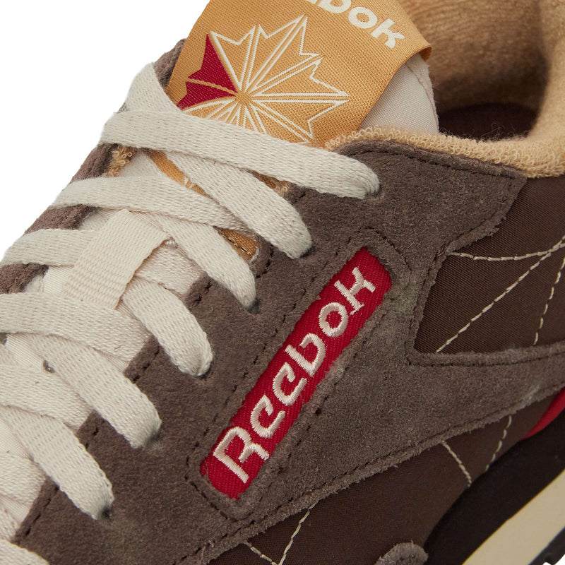 Close-up of brown Reebok Classic Leather Premium LTD Shoes, featuring white laces, a red Reebok logo on the side, and a beige tongue with a red starburst—highlighting the iconic silhouette of these retro sneakers.