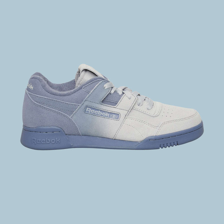 The Reebok Workout Plus OG Shoes in light grey and lavender are shown from the side on a solid light blue background, highlighting their suede and leather textures, classic silhouette, and signature Reebok branding on the side.