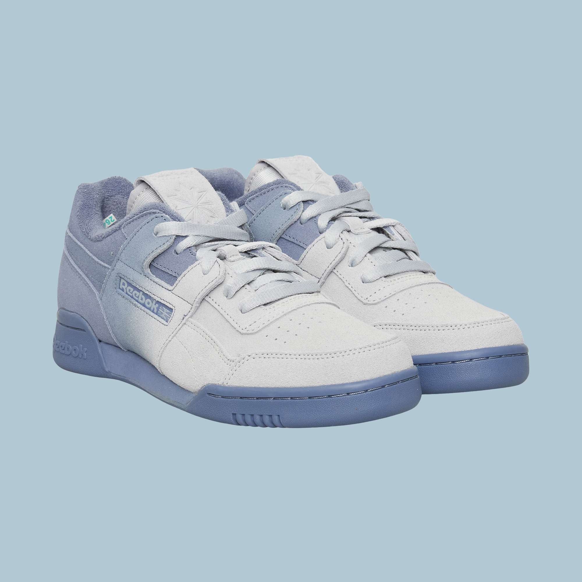 A pair of light grey and blue Reebok Workout Plus OG Shoes with suede texture, blue soles, and laces showcases a classic silhouette against a light blue background.