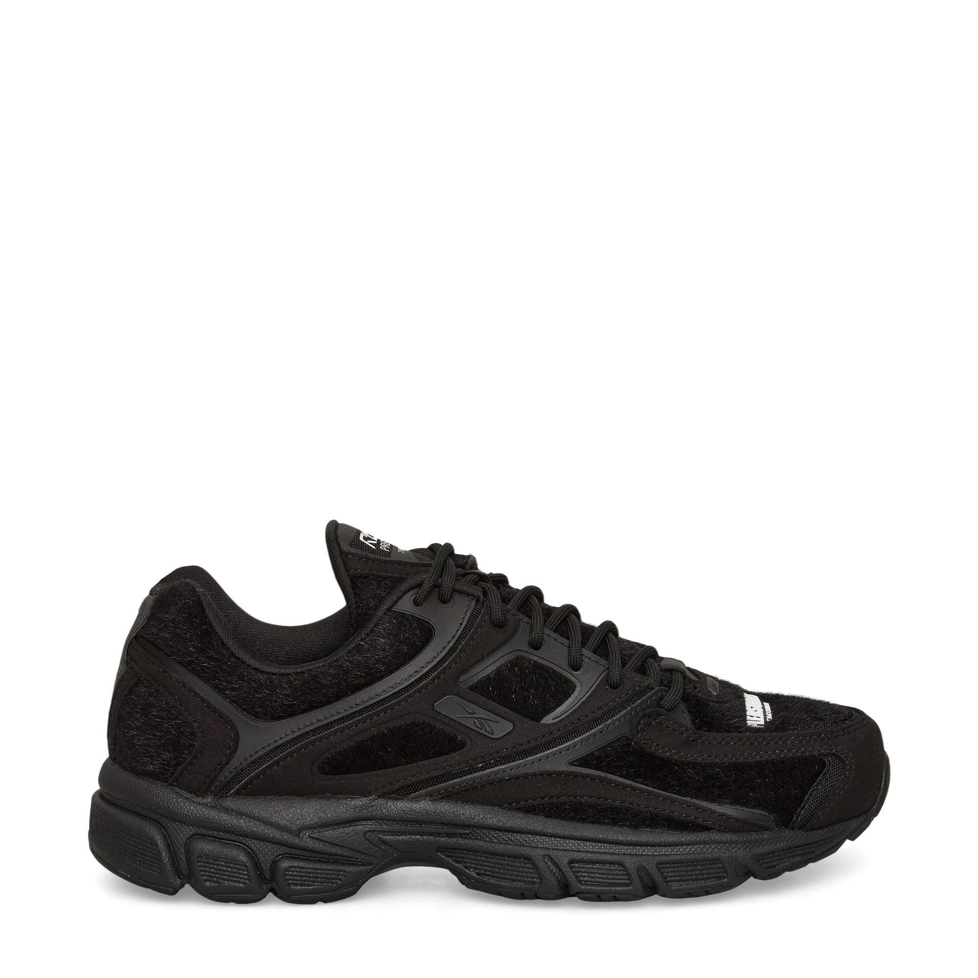 A black athletic sneaker with mesh and suede panels, lace-up closure, textured rubber sole, and subtle branding on the side and tongue, shown in a side profile against a white background.