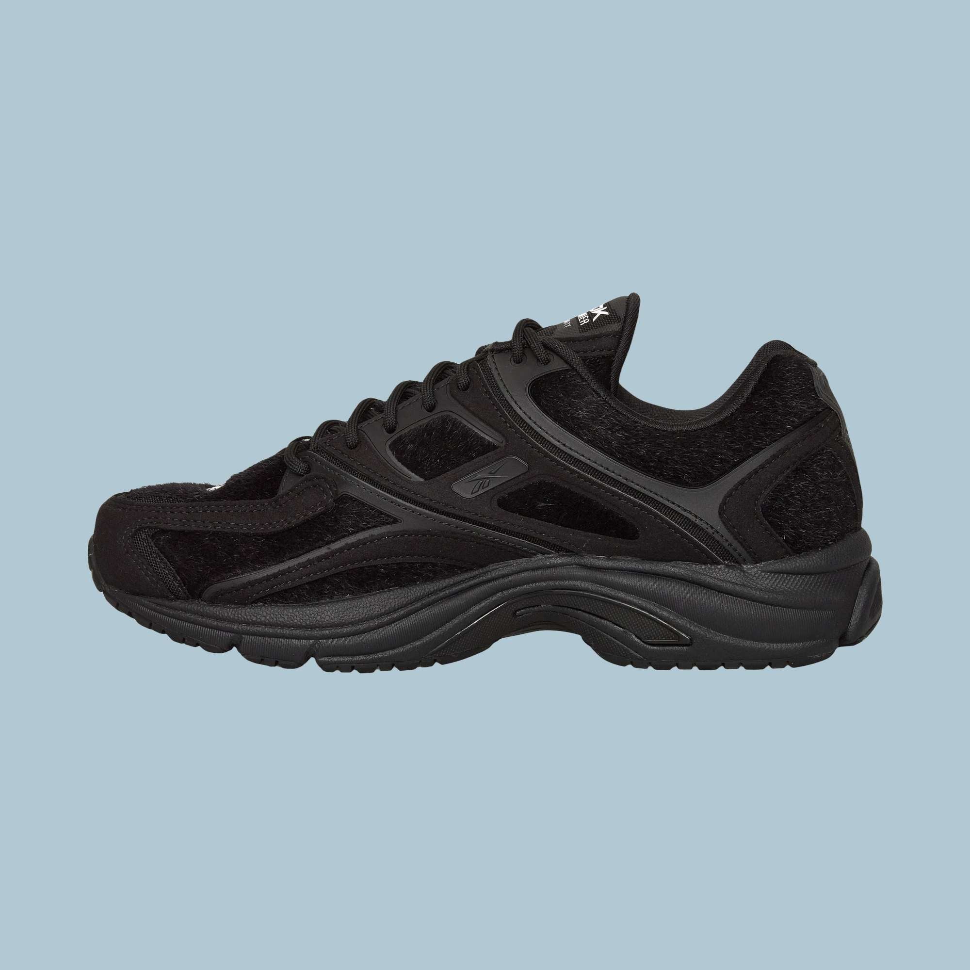 The Reebok Pleasures Premier Trinity KFS Shoes feature a black textured pony hair upper and thick sole, showcased in profile on a light blue background—a striking release from the latest Pleasures collaboration.