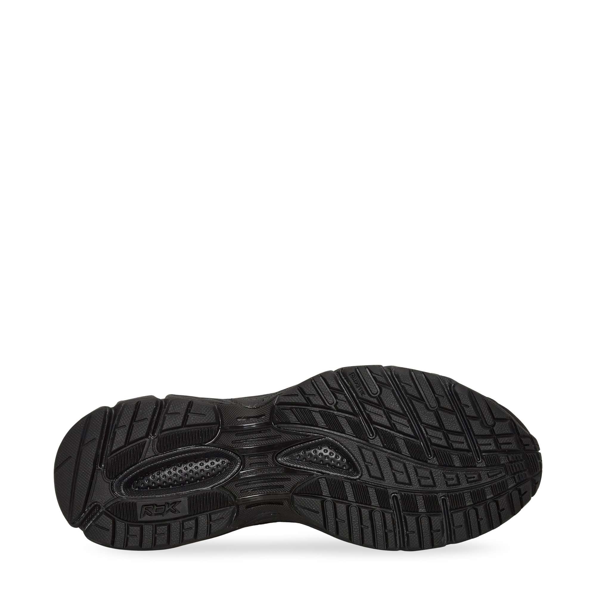 The image shows the black rubber outsole of a shoe, featuring various textured patterns and grooves for traction and support. The sole is viewed from the bottom, displaying details in the tread design.