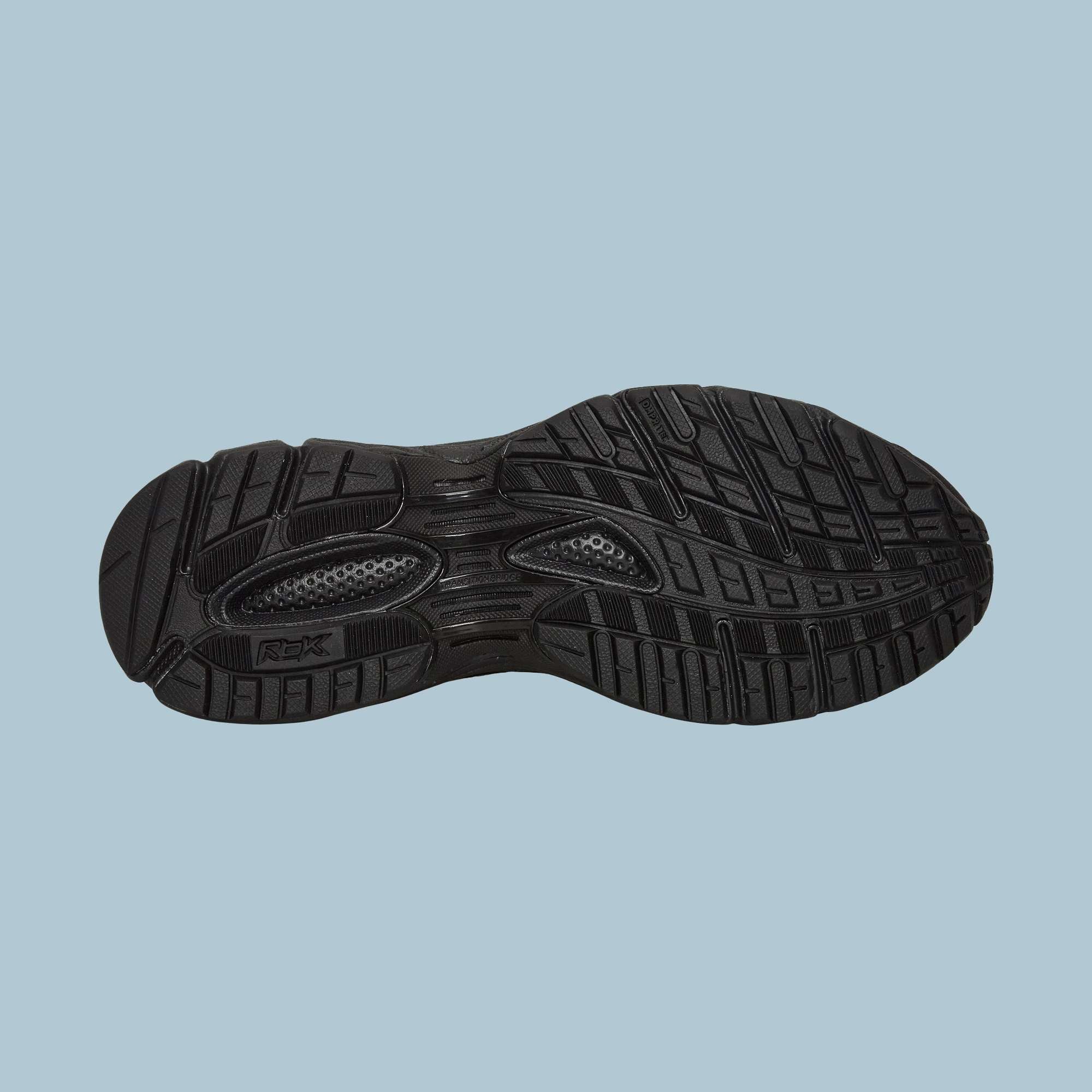 The Reebok Pleasures Premier Trinity KFS Shoes feature a black rubber sole with textured tread for grip, grooves, and raised sections for traction. Photographed on a light blue background, this design is part of a Pleasures collaboration.