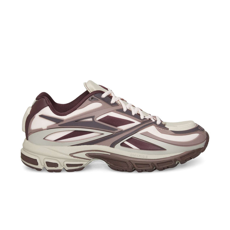 The Reebok Premier Road Modern sneaker features a beige and maroon colorway, dynamic angular patterns, and a thick dual-density midsole for grip. Shown in side profile on a white background.