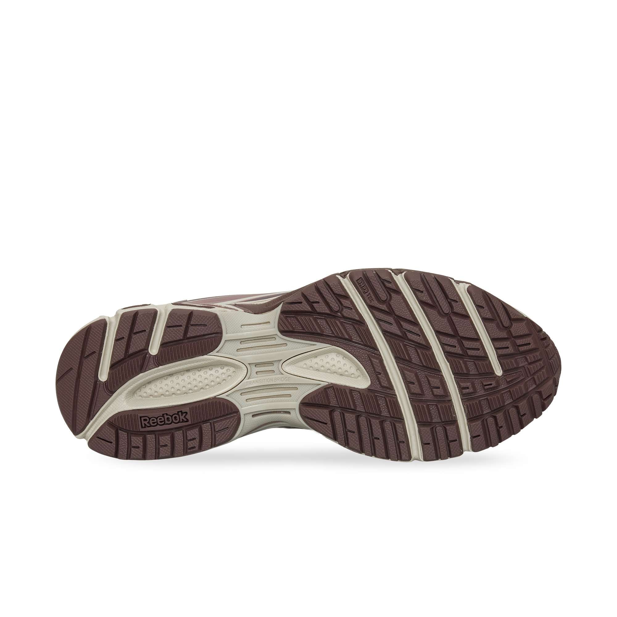 The image displays the outsole of the Reebok Premier Road Modern, showcasing a brown and beige pattern with textured grips for traction, a dual-density midsole for comfort, and the Reebok logo on the sole.