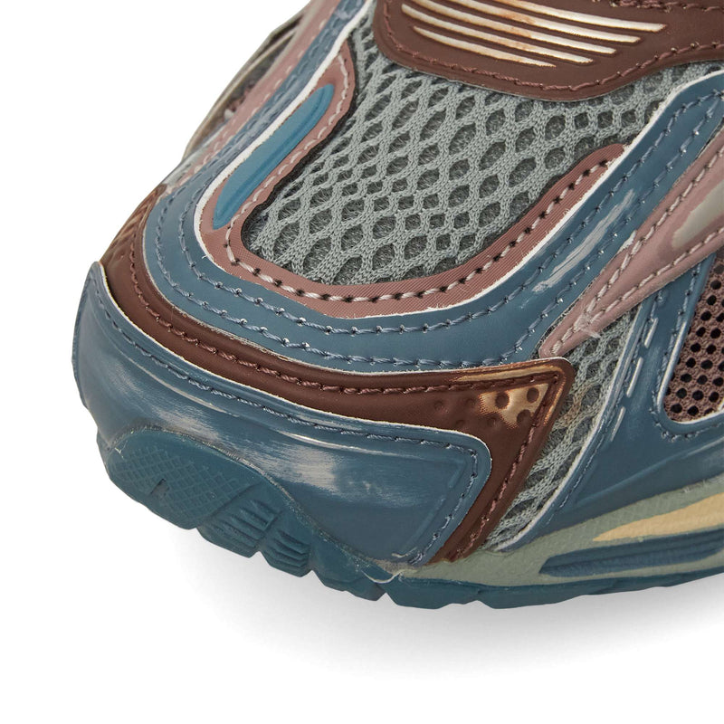 Close-up of the Reebok Premier Road Ultra toe area, showcasing a textured blue, brown, and gray design with mesh and layered synthetics, visible stitching, dual-density midsole detail, and treaded sole.