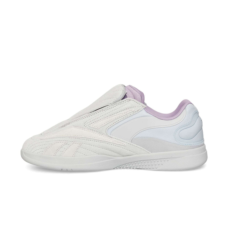 The Reebok Hammer Pro Ltd is a white slip-on sneaker with light grey and pale lavender accents, featuring a durable rubber sole, suede upper, textured sole, and curved stitching details on the side.