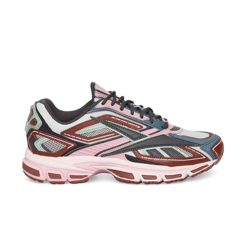 The Reebok Premier Road Ultra is a stylish sneaker in pink, maroon, gray, and black with mesh panels, detailed overlays, and a dual-density midsole—shown in side profile against a white background.