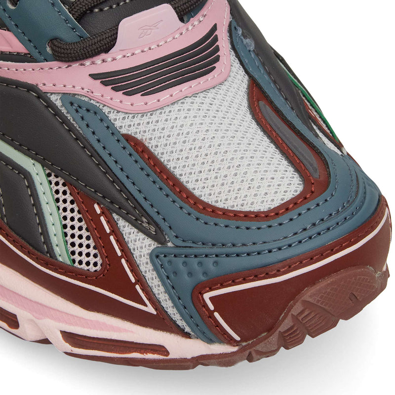 Close-up of the Reebok Premier Road Ultra, a retro running sneaker with blue, red, pink, and black layered panels on white mesh, detailed textures and stitching, and a dual-density midsole for comfort.