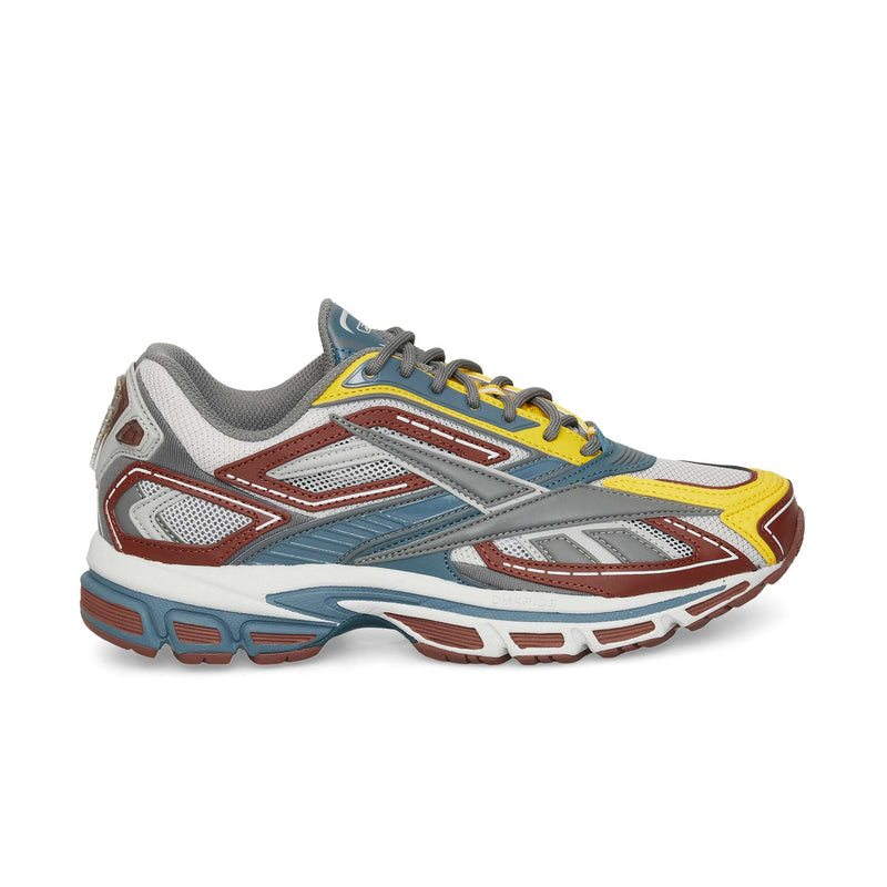 The Reebok Premier Road Ultra is a vibrant running sneaker with gray, white, yellow, and brown mesh and synthetic panels, blue accents, a multi-colored thick sole, and dual-density midsole. Side profile shown on white background.