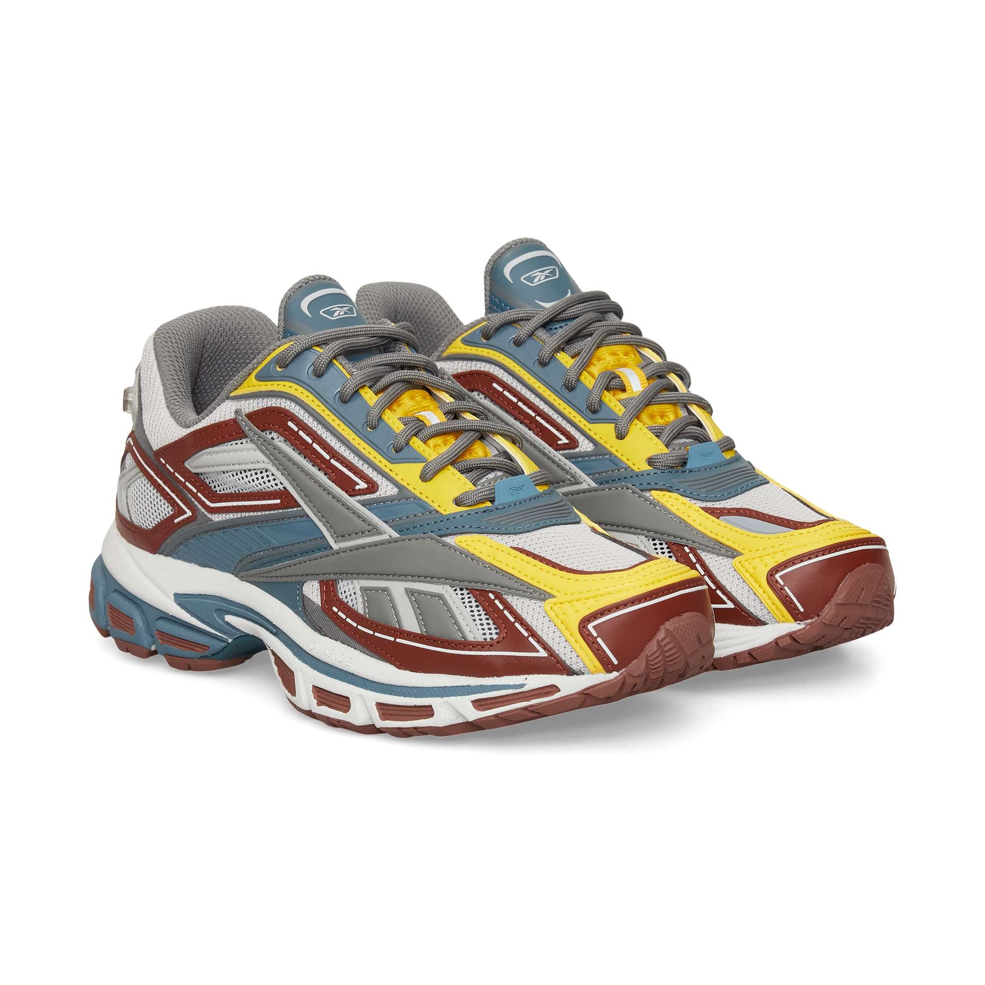The Reebok Premier Road Ultra sneakers feature multicolored yellow, red, gray, white, and blue accents, a dual-density midsole, and gray laces, shown against a white background.