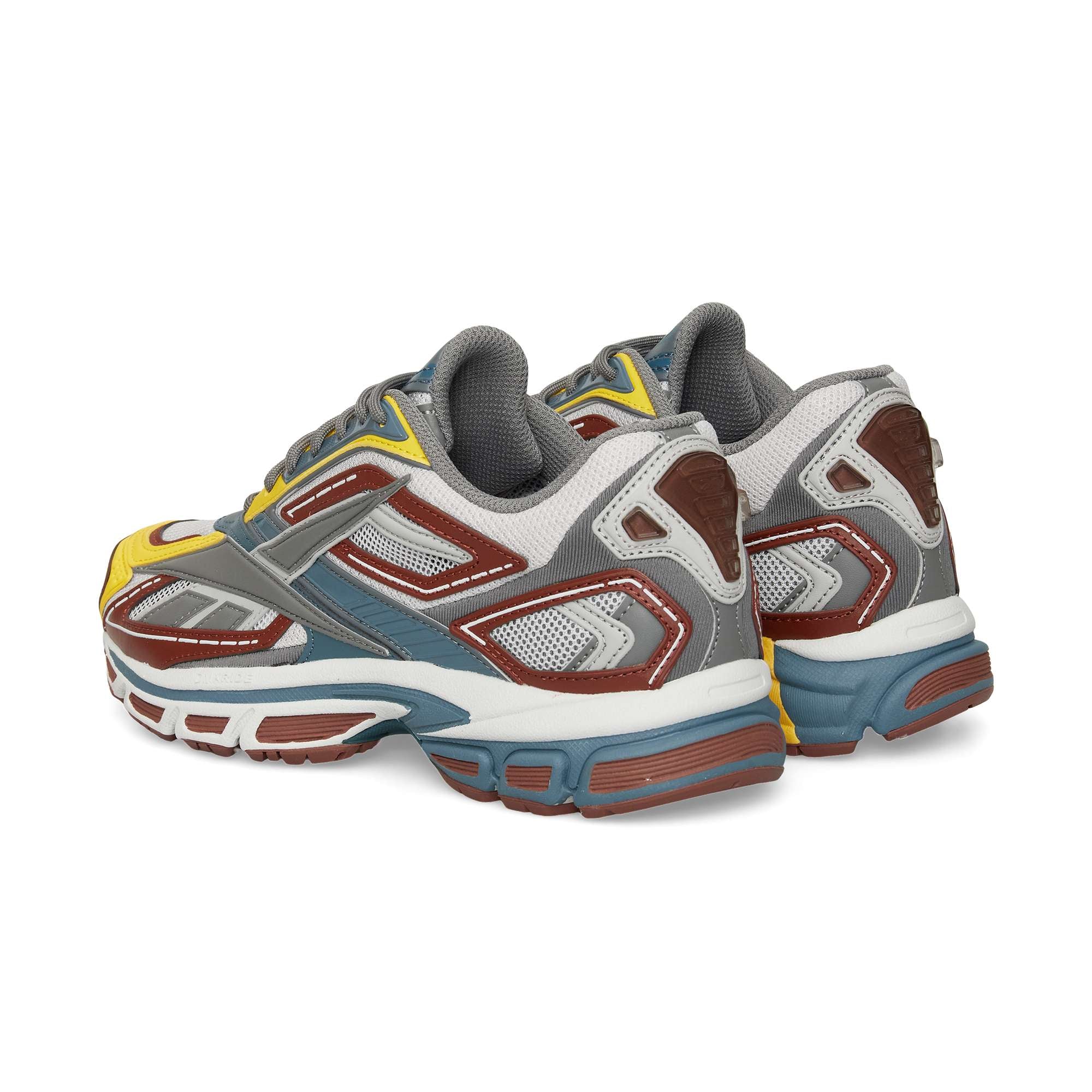 A pair of Reebok Premier Road Ultra sneakers featuring multicolored yellow, brown, gray, white, and blue accents are shown side by side, highlighting the backs and sides of these archival running shoes.