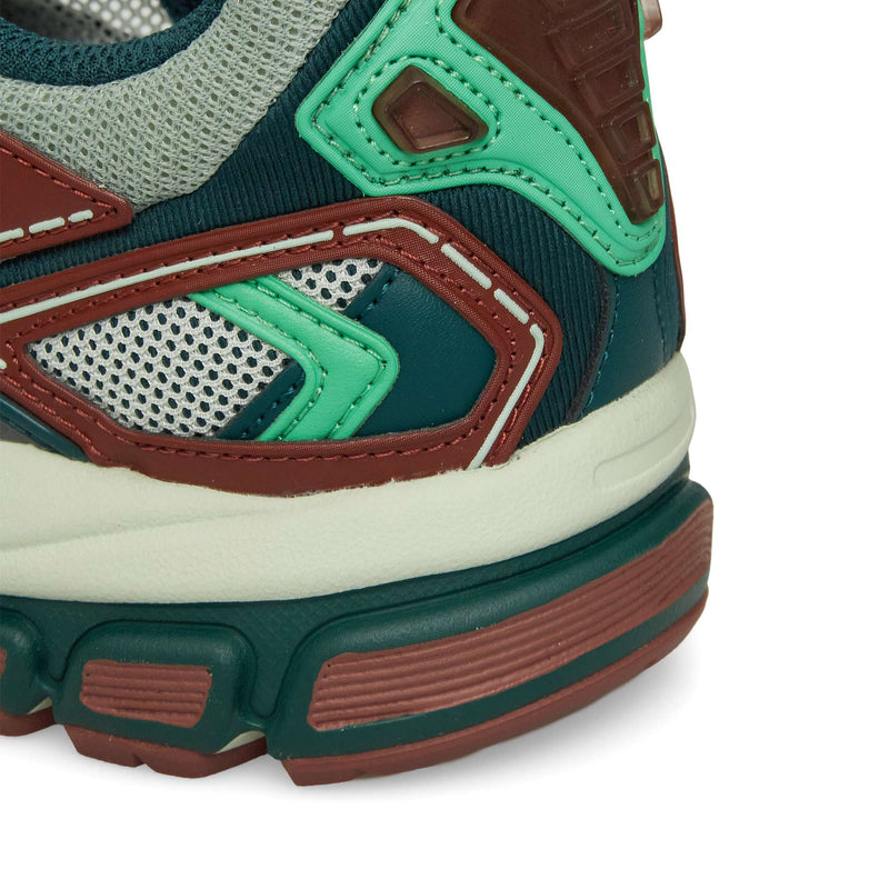 Close-up of the Reebok Premier Road Ultra heel and midsole, showcasing green, brown, off-white, and grey colors with mesh and synthetic overlays, intricate stitching, and a dual-density midsole.