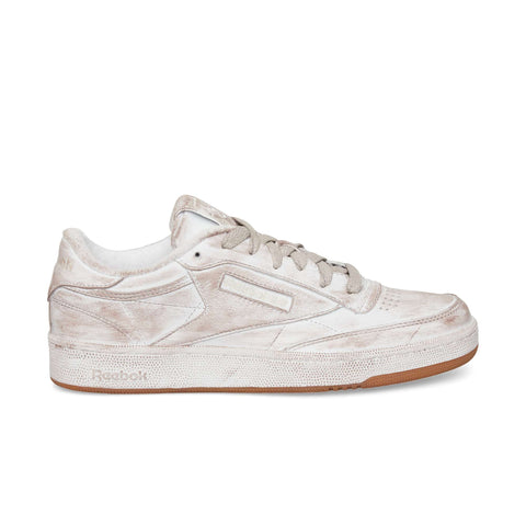 The Reebok Club C 85 Vintage in beige and white features a worn, distressed finish, light beige laces, and a brown rubber sole—shown from the side against a white background, it’s a true lifestyle classic.