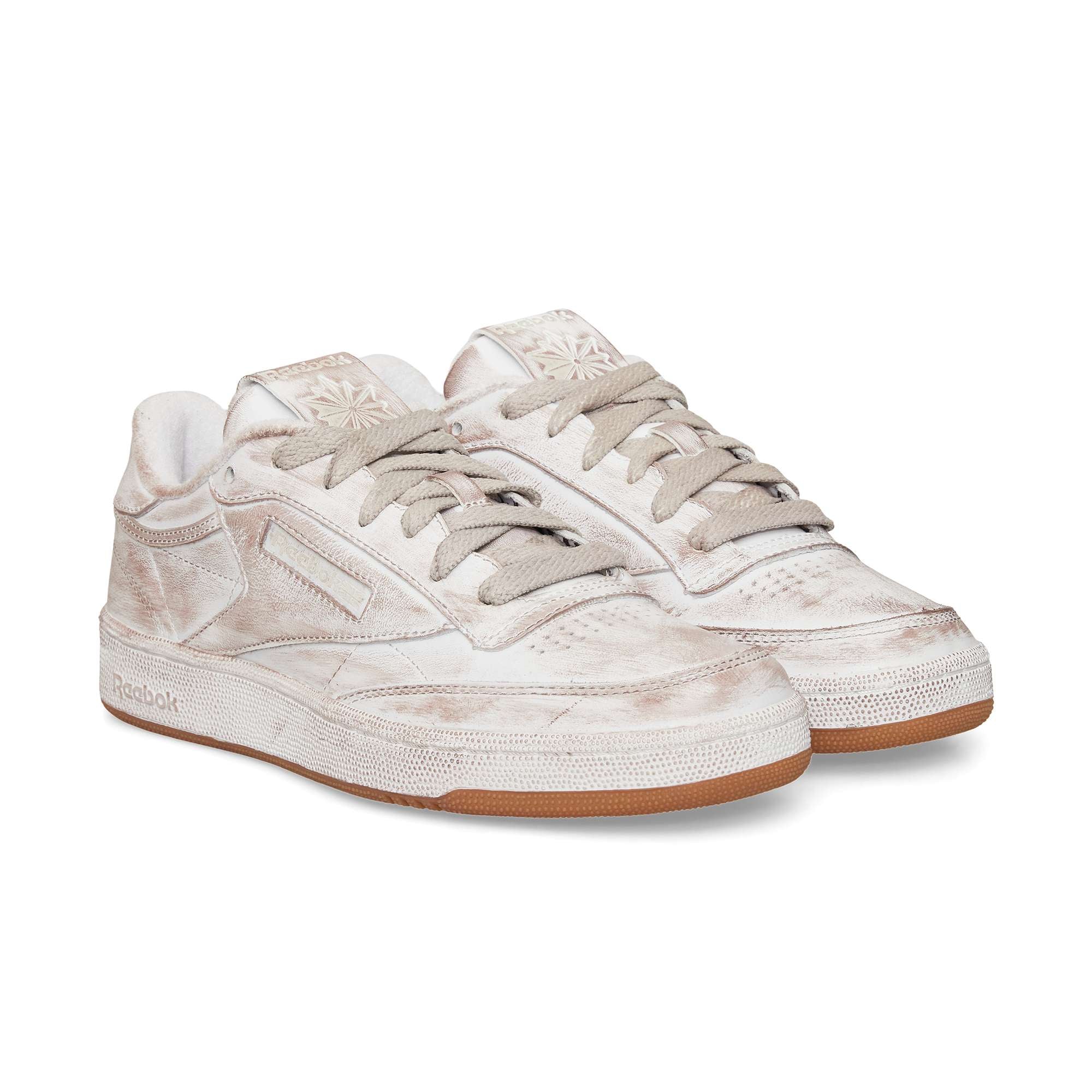 A pair of beige Reebok Club C 85 Vintage sneakers with tied laces, a slightly distressed finish, and gum soles—an iconic classic—are positioned side by side on a white background.