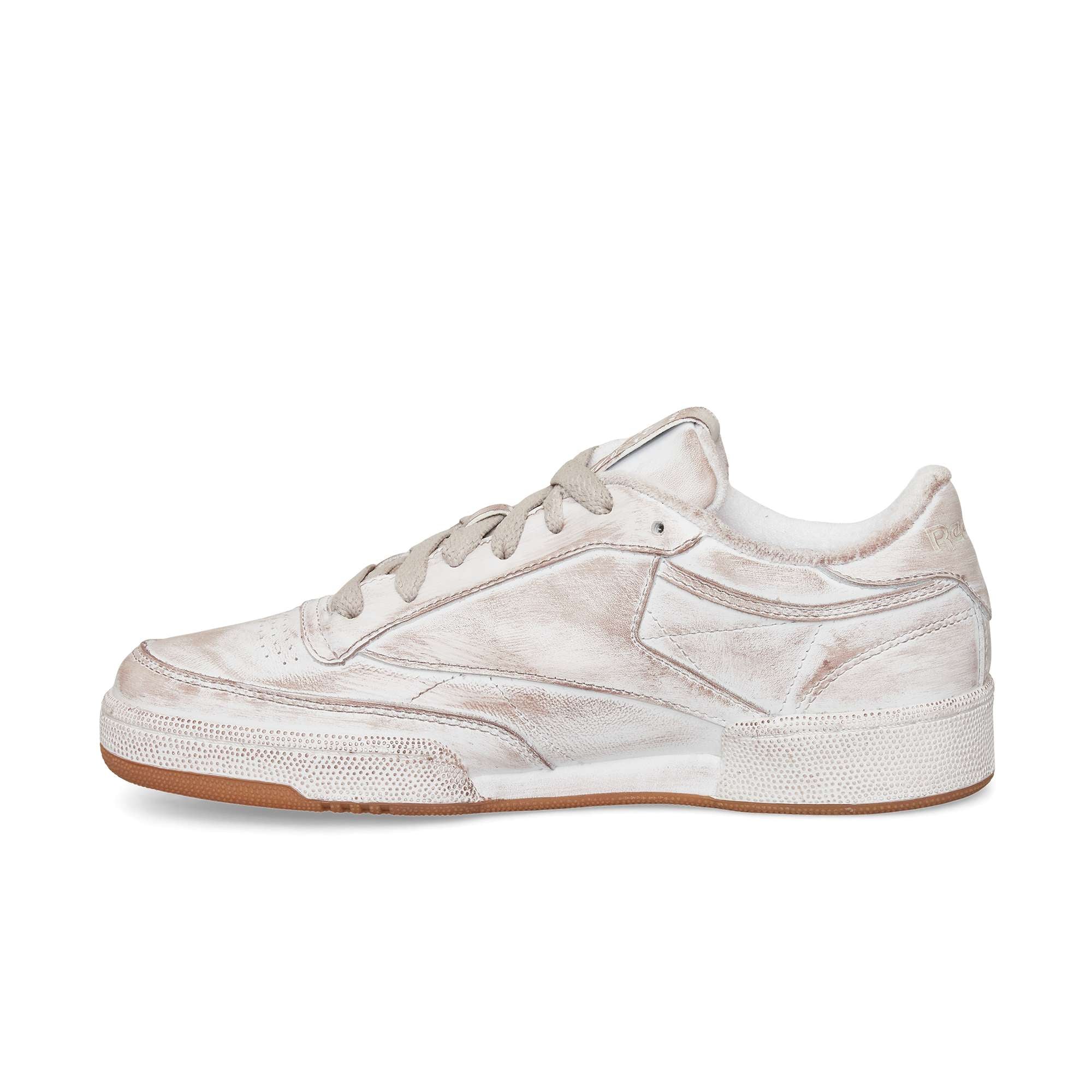 A side view of the Reebok Club C 85 Vintage, a low-top sneaker with a worn white finish, gray laces, textured leather details, and a brown rubber sole. The distressed look adds timeless appeal to this classic tennis-inspired design.