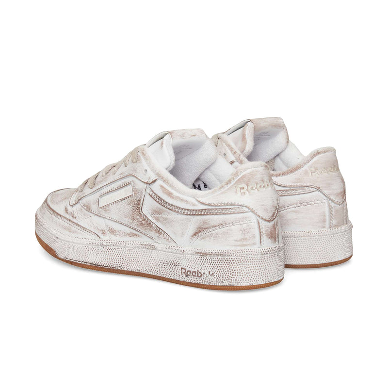 The Reebok Club C 85 Vintage sneakers feature an off-white upper, distressed textured details, and light brown rubber soles, shown at an angle highlighting the back and sides—a true lifestyle classic.
