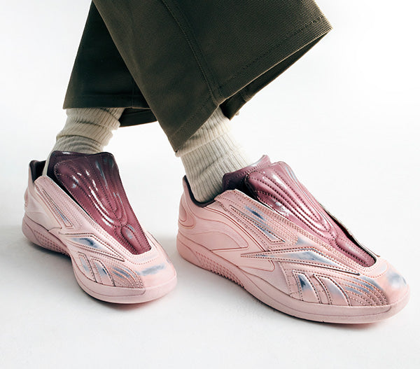 Pink slip-on shoes worn with white socks and green pants on a light background