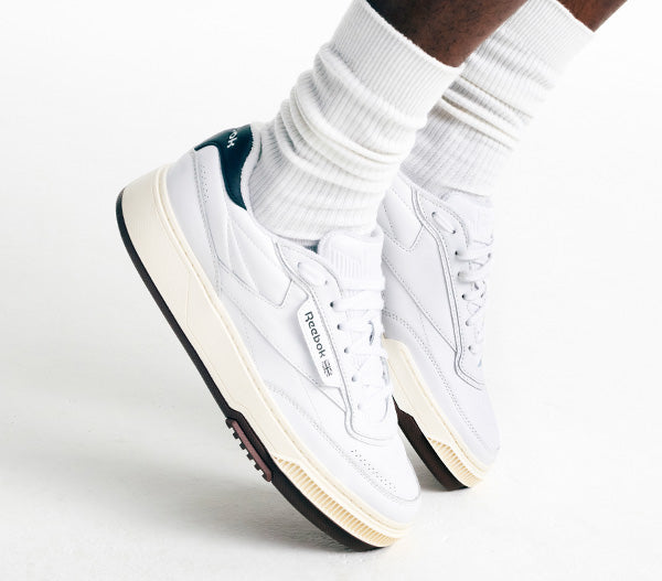White sneakers with black soles worn with white socks on a light gray background