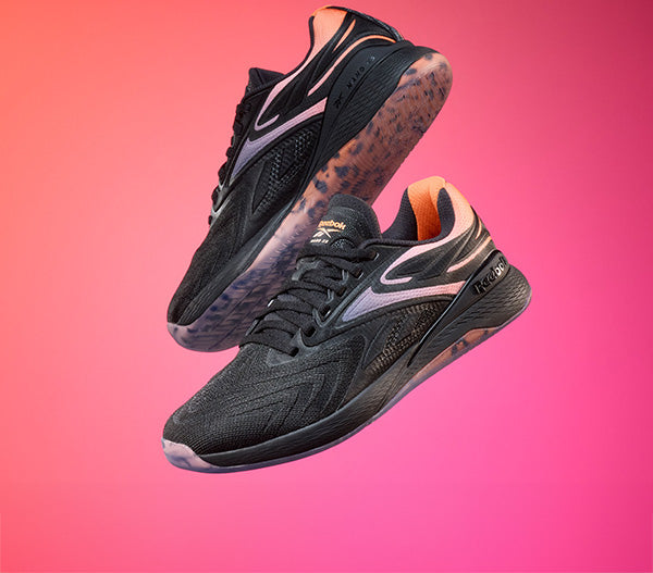 Black athletic shoes with pink accents on a gradient pink background