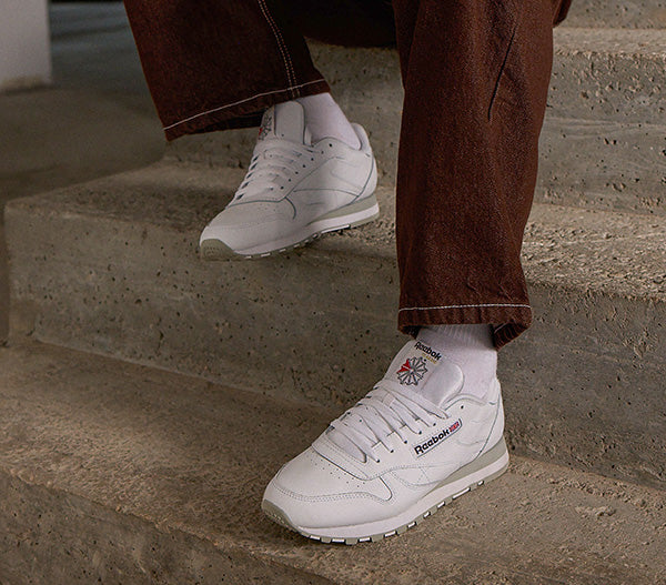 White sneakers with Reebok logo worn on concrete steps