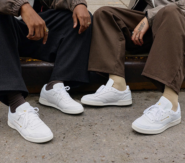 two people wearing white sneakers sitting on a bench