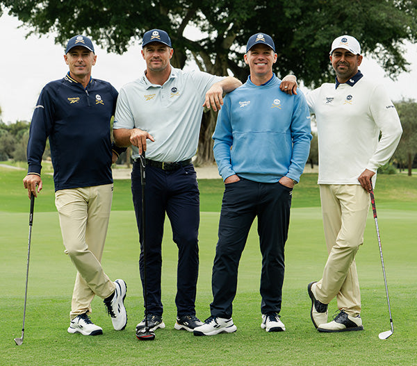 Four men posing together on a golf course with golf clubs.