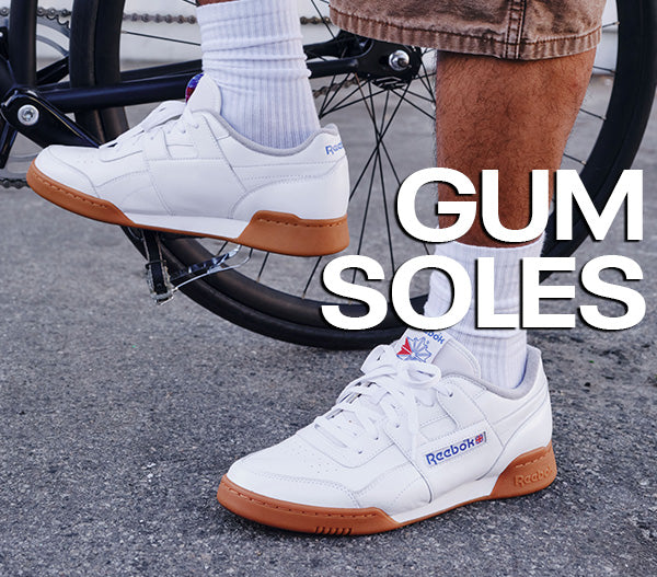White sneakers with brown soles worn by a person on a bike, with 'GUM SOLES' text overlay.
