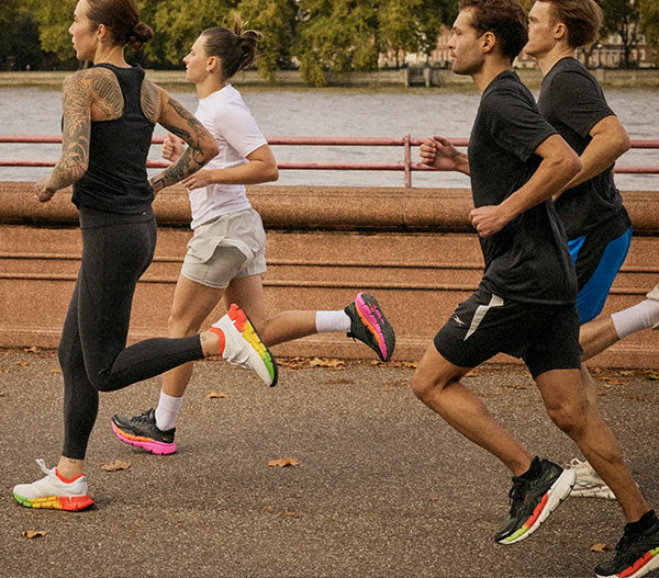 Four runners in athletic gear running along a path by a waterfront.