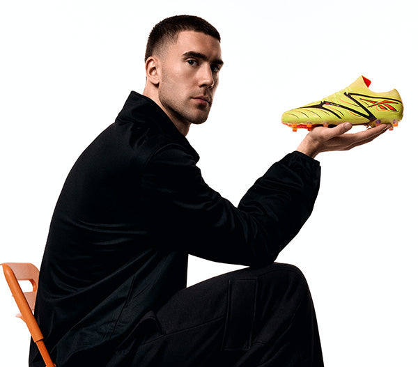 Man holding a yellow soccer shoe against a white background